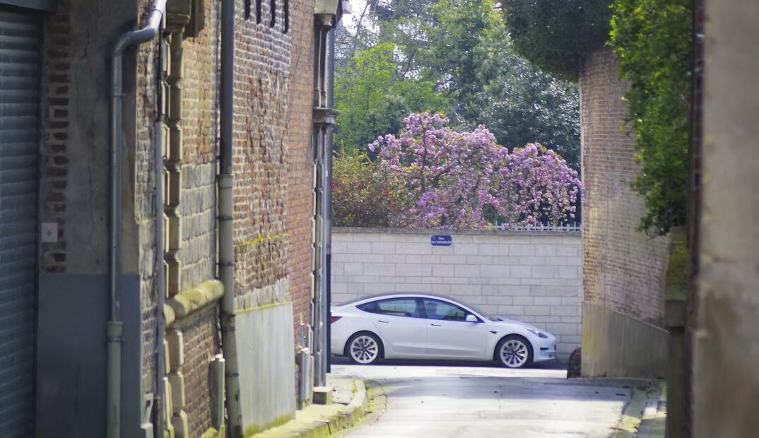 Voiture électrique blanche garée au bout d'une ruelle entre des murs de brique