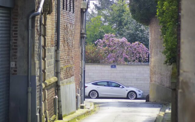 Voiture électrique blanche garée au bout d'une ruelle entre des murs de brique