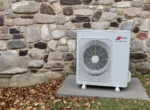 Unité extérieure de pompe à chaleur air-eau installée contre le mur d'une maison en pierre