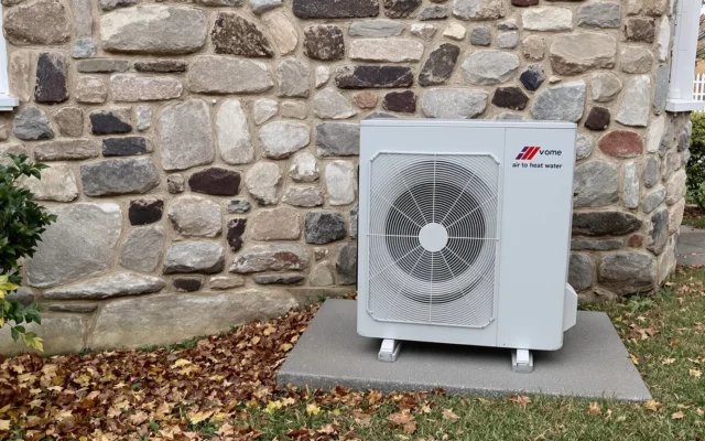 Unité extérieure de pompe à chaleur air-eau installée contre le mur d'une maison en pierre